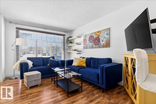 Bright living area featuring wood-finish flooring, a large window with blinds, and white walls - 18 6032 38 Avenue, Edmonton, AB - Indoor Photo Showing Living Room