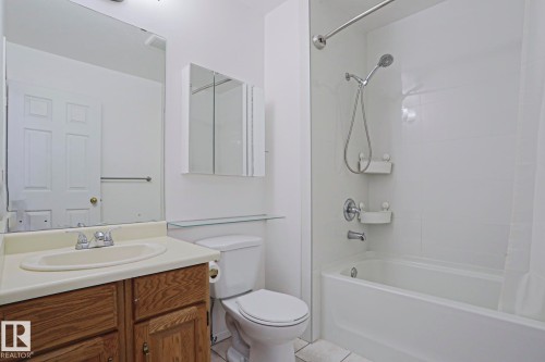Full bathroom featuring a tub and shower combination with a curved shower rod, a wood-finish vanity with an integrated sink, a large wall mirror, and a wall-mounted medicine cabinet - 2433 89 Street, Edmonton, AB - Indoor Photo Showing Bathroom