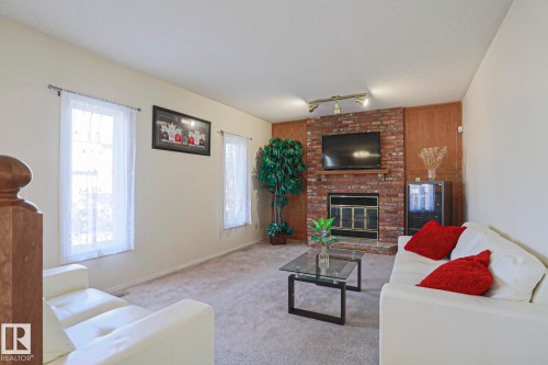Living area featuring a brick fireplace surround with a metal firebox, wood paneling, and track lighting - 2433 89 Street, Edmonton, AB - Indoor Photo Showing Living Room With Fireplace
