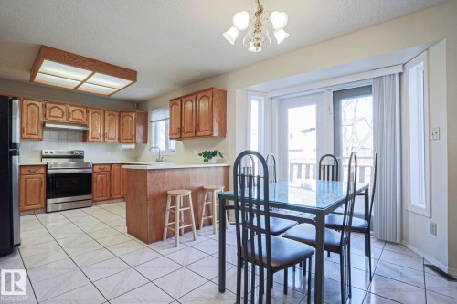 Eat-in kitchen featuring wood cabinetry, stainless steel appliances, and a breakfast bar - 2433 89 Street, Edmonton, AB - Indoor