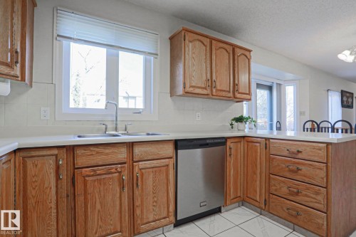 Kitchen featuring light wood cabinetry, white countertops, white tiled backsplash, and stainless steel dishwasher - 2433 89 Street, Edmonton, AB - Indoor Photo Showing Kitchen With Double Sink