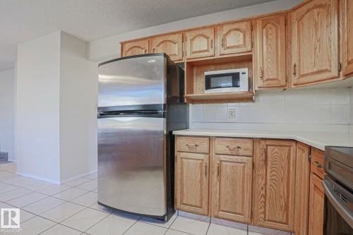 Kitchen featuring a stainless steel refrigerator, wood cabinetry, white countertops, tile backsplash, and tile flooring - 2433 89 Street, Edmonton, AB - Indoor Photo Showing Kitchen