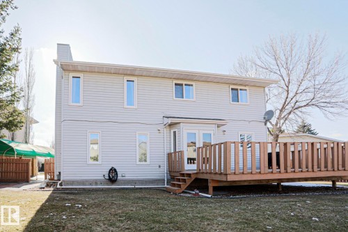 Rear exterior featuring light-colored siding, a multi-level wood deck, and a grass lawn - 2433 89 Street, Edmonton, AB - Outdoor With Deck Patio Veranda With Exterior
