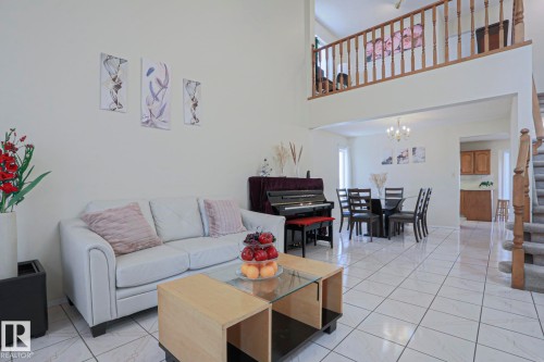 Open-concept living area featuring high ceilings, white tile flooring, a dining area with chandelier lighting, and a staircase with wood railings and carpeted treads - 2433 89 Street, Edmonton, AB - Indoor Photo Showing Living Room