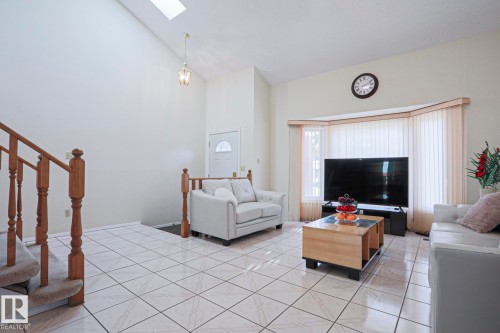 Living area featuring tiled flooring, a prominent bay window with vertical blinds, and a vaulted ceiling with a skylight - 2433 89 Street, Edmonton, AB - Indoor
