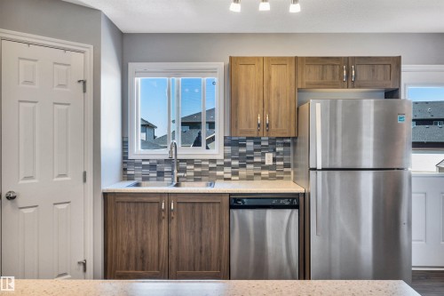 Kitchen featuring wood-finish cabinetry, stainless steel appliances, a multi-tone tile backsplash, and a double-basin sink - 2424 Wonnacott Crest, Edmonton, AB - Indoor Photo Showing Kitchen With Stainless Steel Kitchen With Double Sink