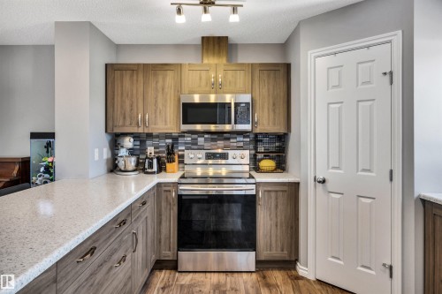 Kitchen featuring wood-finish cabinetry, stainless steel appliances, speckled countertops, and a mosaic tile backsplash - 2424 Wonnacott Crest, Edmonton, AB - Indoor Photo Showing Kitchen