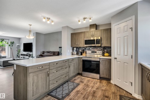 Kitchen featuring wood-finish flooring, light wood-grain cabinetry, stainless steel appliances, a tiled backsplash, and light-colored countertops - 2424 Wonnacott Crest, Edmonton, AB - Indoor Photo Showing Kitchen