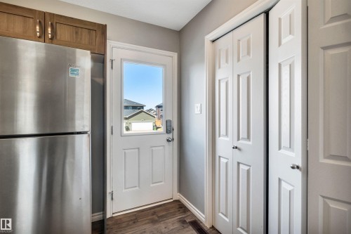 Stainless steel refrigerator with overhead wood-finish cabinetry, a white door with a window pane, and wood-finish flooring - 2424 Wonnacott Crest, Edmonton, AB - Indoor Photo Showing Other Room