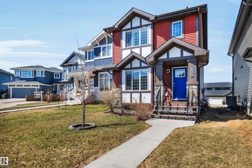 Red and white exterior featuring a front entry with a bright blue door, stone pillar accents, and a covered porch - 2424 Wonnacott Crest, Edmonton, AB - Outdoor With Facade