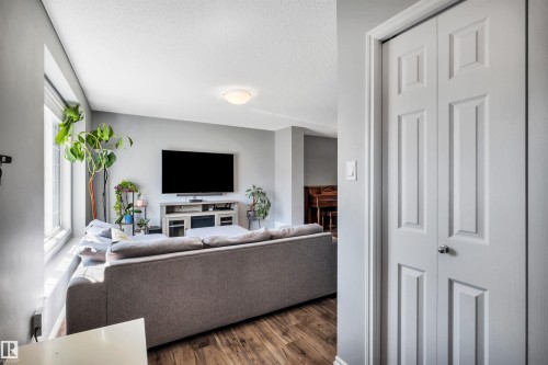 Living area featuring wood-finish flooring, a large window, a wall-mounted television, and a flush-mount ceiling light - 2424 Wonnacott Crest, Edmonton, AB - Indoor