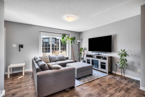 Living area featuring wood-finish flooring, a large picture window, light grey wall paint, and a ceiling-mounted light fixture - 2424 Wonnacott Crest, Edmonton, AB - Indoor Photo Showing Living Room