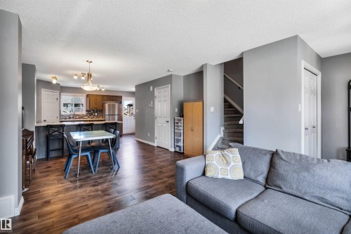 Open-concept living area featuring wood-finish flooring, a kitchen with stainless steel appliances, a breakfast bar, and a dining area with pendant lighting - 2424 Wonnacott Crest, Edmonton, AB - Indoor Photo Showing Living Room