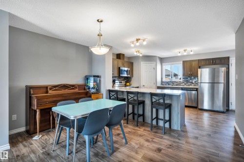 Open-concept kitchen and dining area featuring wood-finish flooring, contemporary light fixtures, and a kitchen island with seating - 2424 Wonnacott Crest, Edmonton, AB - Indoor