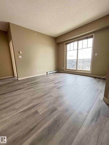 Spacious interior featuring wide-plank wood-finish flooring, neutral wall tones, and a large window with a balcony - 408 111 Ambelside Drive Sw, Edmonton, AB - Indoor Photo Showing Other Room