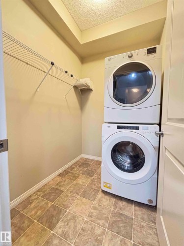 Laundry area featuring durable tile flooring, stackable appliances, integrated wire shelving, and neutral wall tones - 408 111 Ambelside Drive Sw, Edmonton, AB - Indoor Photo Showing Laundry Room