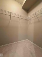 Walk-in closet featuring built-in wire shelving, neutral-toned walls, textured ceiling, light-colored carpeting, and white baseboards - 