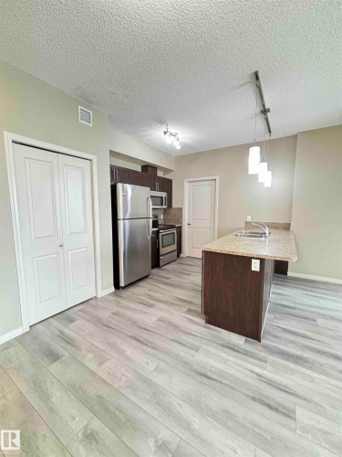 Modern kitchen area featuring light wood-finish flooring, stainless steel appliances, and a central island with a double basin sink - 408 111 Ambelside Drive Sw, Edmonton, AB - Indoor Photo Showing Kitchen