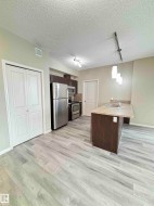 Modern kitchen area featuring light wood-finish flooring, stainless steel appliances, and a central island with a double basin sink - 
