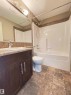 Contemporary bathroom featuring a dark wood-finish vanity with an integrated sink, a full vanity mirror, and a white tub and shower combination - 408 111 Ambelside Drive Sw, Edmonton, AB  - Indoor Photo Showing Bathroom 