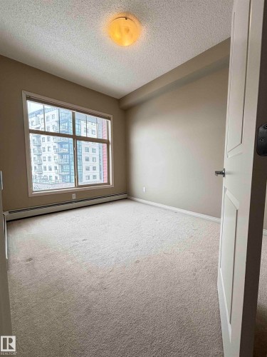 Spacious interior room featuring a large window, neutral wall tones, textured ceiling, and carpeted flooring - 408 111 Ambelside Drive Sw, Edmonton, AB - Indoor Photo Showing Other Room