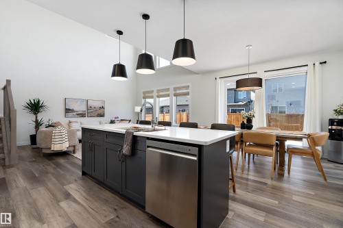 Kitchen island with dark cabinetry, white countertop, and stainless steel dishwasher - 591 Boulder Wynd, Leduc, AB - Indoor Photo Showing Kitchen With Upgraded Kitchen