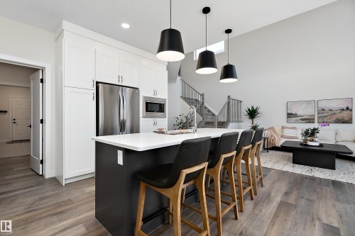 Modern kitchen featuring a large island with seating, stainless steel appliances, white cabinetry, and wood-finish flooring - 591 Boulder Wynd, Leduc, AB - Indoor