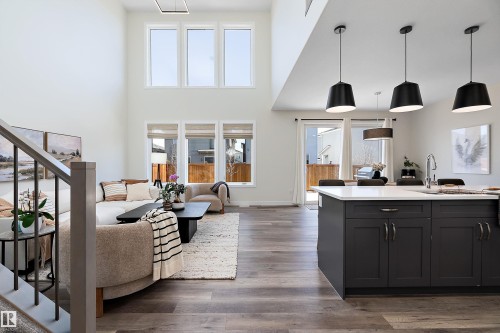 Open-concept living space featuring wood-finish flooring throughout, a kitchen island with dark cabinetry and a light-colored countertop, and a dining area with pendant lighting - 591 Boulder Wynd, Leduc, AB - Indoor