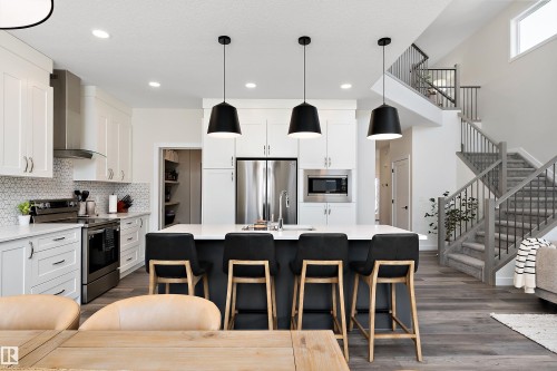 Open-concept kitchen featuring an oversized island, stainless steel appliances, white cabinetry, and wood-finish flooring - 591 Boulder Wynd, Leduc, AB - Indoor Photo Showing Kitchen With Upgraded Kitchen