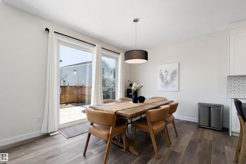 Spacious dining area featuring wood-finish flooring, a contemporary drum pendant light, and a white tile backsplash - 591 Boulder Wynd, Leduc, AB - Indoor Photo Showing Dining Room