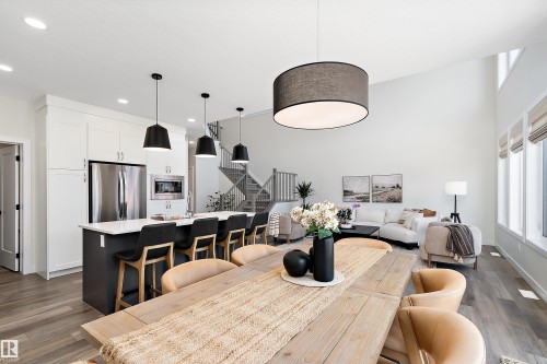 Open-concept living space featuring high ceilings, wood-finish flooring, a contemporary kitchen island with seating, stainless steel appliances, and a staircase with open risers - 591 Boulder Wynd, Leduc, AB - Indoor Photo Showing Dining Room