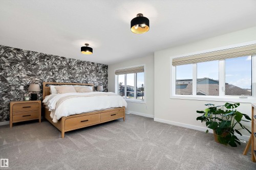 Spacious room featuring a prominent accent wall with a botanical pattern, two large windows, and overhead flush-mount lighting fixtures - 591 Boulder Wynd, Leduc, AB - Indoor Photo Showing Bedroom