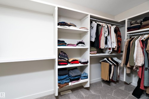 Walk-in closet featuring white built-in shelving, multiple hanging rods, and light gray patterned carpeting - 591 Boulder Wynd, Leduc, AB - Indoor With Storage