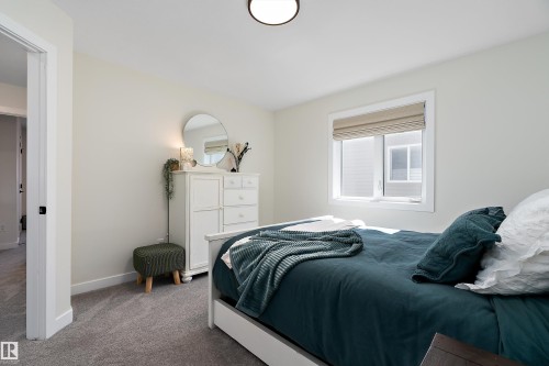 Bright bedroom featuring light-toned walls, grey carpet, a modern flush-mount ceiling light, and a white-framed window with a roman shade - 591 Boulder Wynd, Leduc, AB - Indoor Photo Showing Bedroom