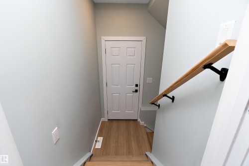 Entryway featuring a paneled door with contemporary hardware, wood-finish flooring, and a light wood-tone handrail with matte black brackets - 591 Boulder Wynd, Leduc, AB - Indoor Photo Showing Other Room