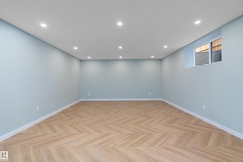 Spacious room featuring wood-finish flooring in a herringbone pattern, light blue walls, recessed lighting, and a single egress window - 591 Boulder Wynd, Leduc, AB - Indoor Photo Showing Other Room