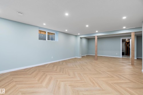 Spacious room featuring light blue walls, recessed ceiling lighting, a window with horizontal blinds, and wood-finish flooring with a chevron pattern - 591 Boulder Wynd, Leduc, AB - Indoor