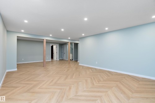 Spacious room featuring wood-finish flooring with a herringbone pattern, light blue walls, white baseboards, and recessed ceiling lighting - 591 Boulder Wynd, Leduc, AB - Indoor Photo Showing Other Room