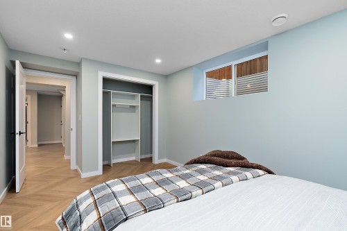 Bedroom featuring light blue walls, recessed lighting, a window with a window well, wood-finish flooring in a herringbone pattern, and an open closet with built-in shelving - 591 Boulder Wynd, Leduc, AB - Indoor Photo Showing Bedroom