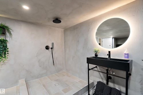 Contemporary bathroom featuring a black floating vanity, circular backlit mirror, black matte fixtures, recessed lighting, and large format floor tiles - 591 Boulder Wynd, Leduc, AB - Indoor