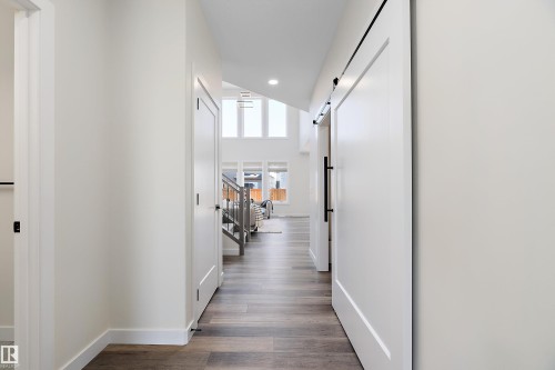 Hallway featuring wood-finish flooring, recessed lighting, white walls, and a modern barn door with black hardware - 591 Boulder Wynd, Leduc, AB - Indoor Photo Showing Other Room