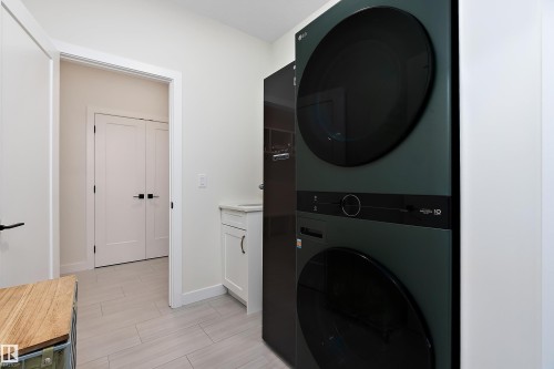 Laundry area featuring a stacked appliance unit, light-toned tile flooring, and a white base cabinet with a countertop - 591 Boulder Wynd, Leduc, AB - Indoor Photo Showing Laundry Room