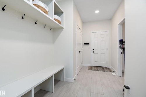 Foyer with light plank-style flooring, white built-in bench, and overhead shelving with black coat hooks - 591 Boulder Wynd, Leduc, AB - Indoor Photo Showing Other Room