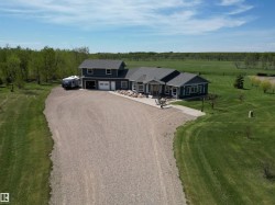 Expansive gravel driveway leading to a multi-level residence featuring dark blue siding, white trim, and a prominent attached two-car garage - 
