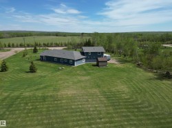 Expansive green lawn with mature evergreen trees, featuring a blue-sided structure with a dark gray shingled roof - 