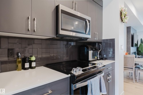 Kitchen featuring contemporary gray cabinetry, stainless steel microwave, white countertops, and a dark tile backsplash - 3288 Keswick Way, Edmonton, AB - Indoor Photo Showing Kitchen With Upgraded Kitchen