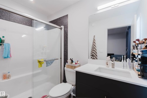 Bathroom featuring a white integrated tub and shower with glass sliding doors, a white toilet, and a vanity with a white countertop and an undermount sink - 3288 Keswick Way, Edmonton, AB - Indoor Photo Showing Bathroom