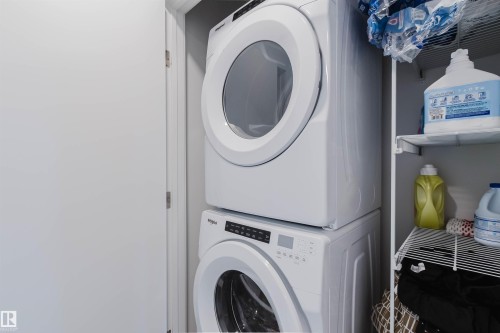 Stacked white front-loading washer and dryer, featuring digital controls and clear viewing windows - 3288 Keswick Way, Edmonton, AB - Indoor Photo Showing Laundry Room