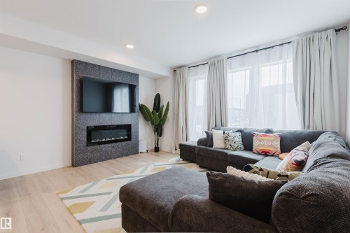 Spacious living area featuring light wood-finish flooring, recessed lighting, and large windows with full-length curtains - 3288 Keswick Way, Edmonton, AB - Indoor Photo Showing Living Room With Fireplace
