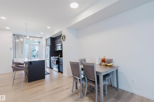 Open-concept living area featuring light wood-finish flooring, recessed lighting, a modern kitchen island with white countertop, and dark-toned cabinetry with stainless steel appliances - 3288 Keswick Way, Edmonton, AB - Indoor Photo Showing Dining Room